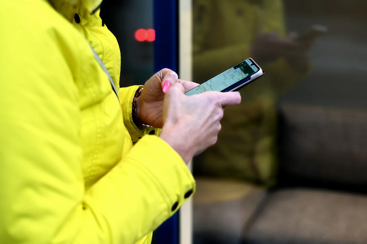 Hands using a smartphone outdoors beside a yellow raincoat.