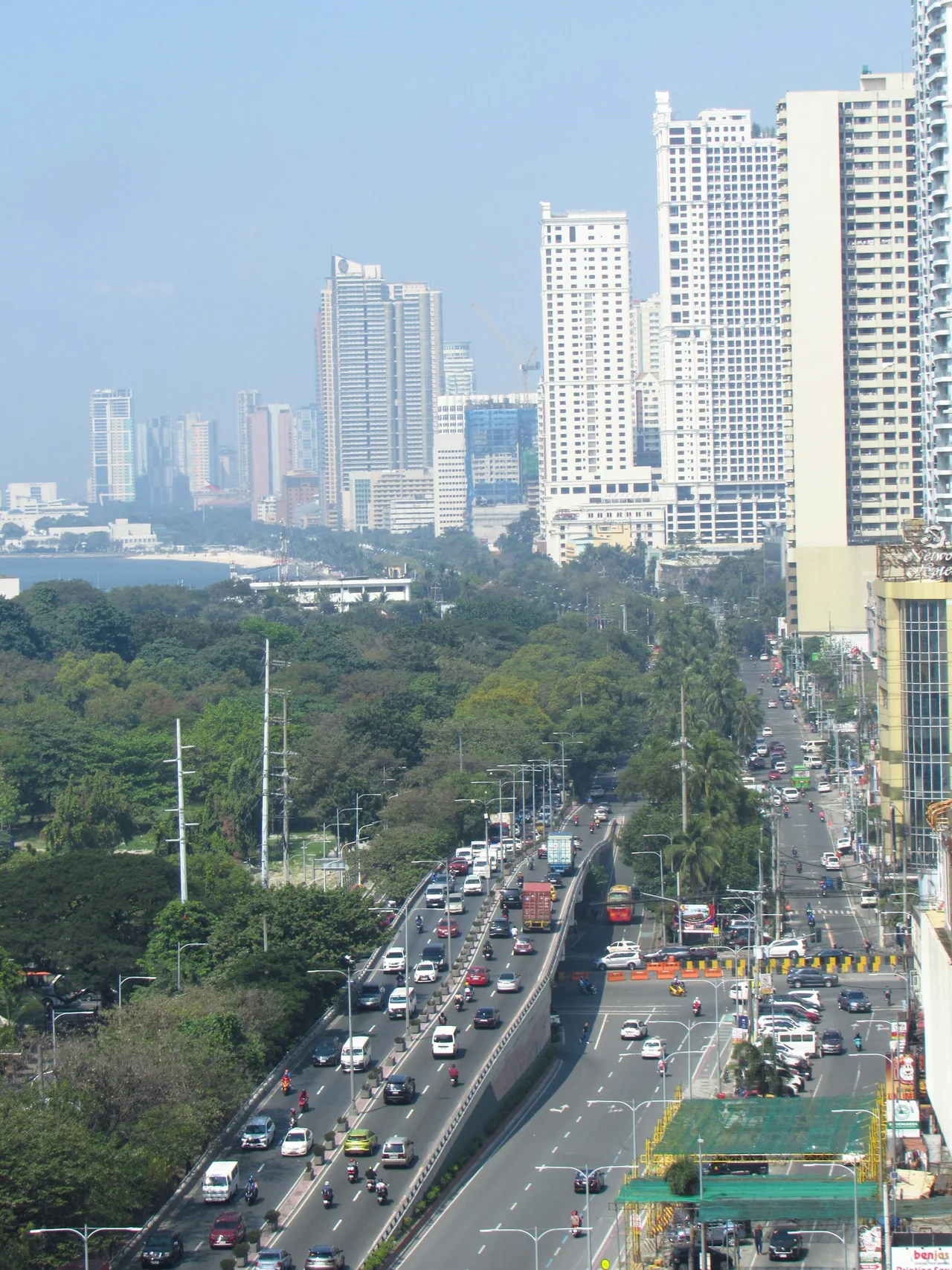 Traffic travels along Roxas Boulevard among buildings and trees in Manila.
