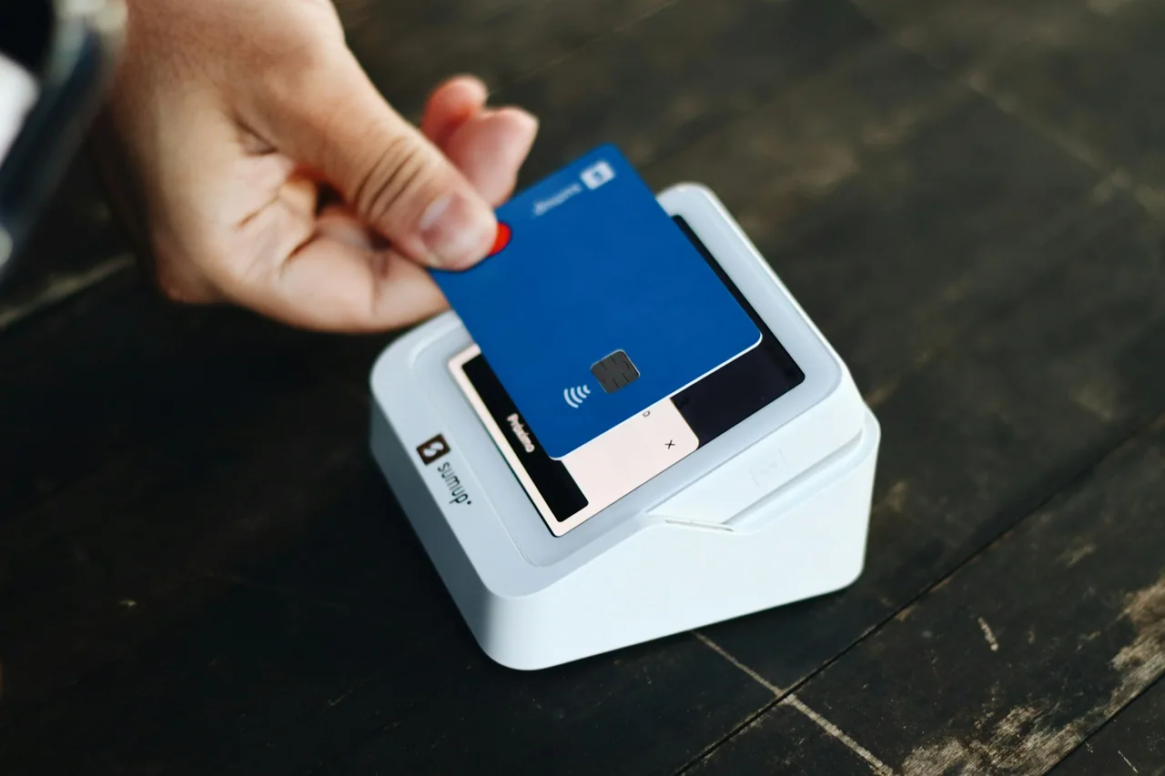 A hand holds a blue payment card over a white card terminal.