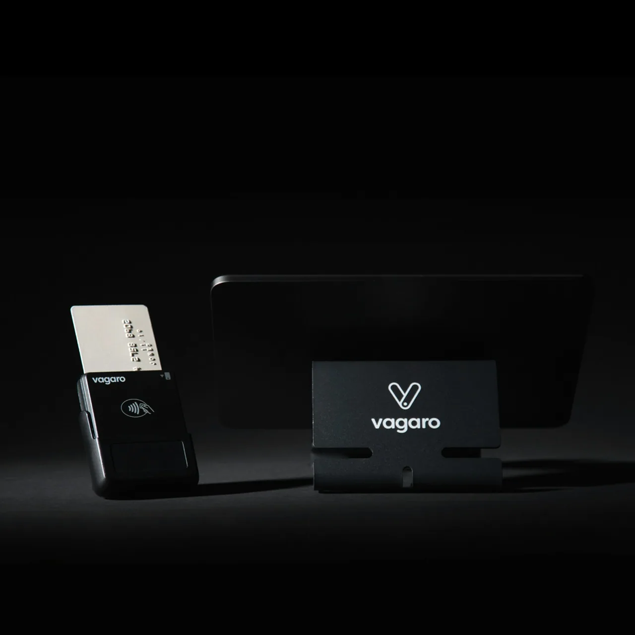 A black card payment terminal with a white card inserted beside a tablet stand.