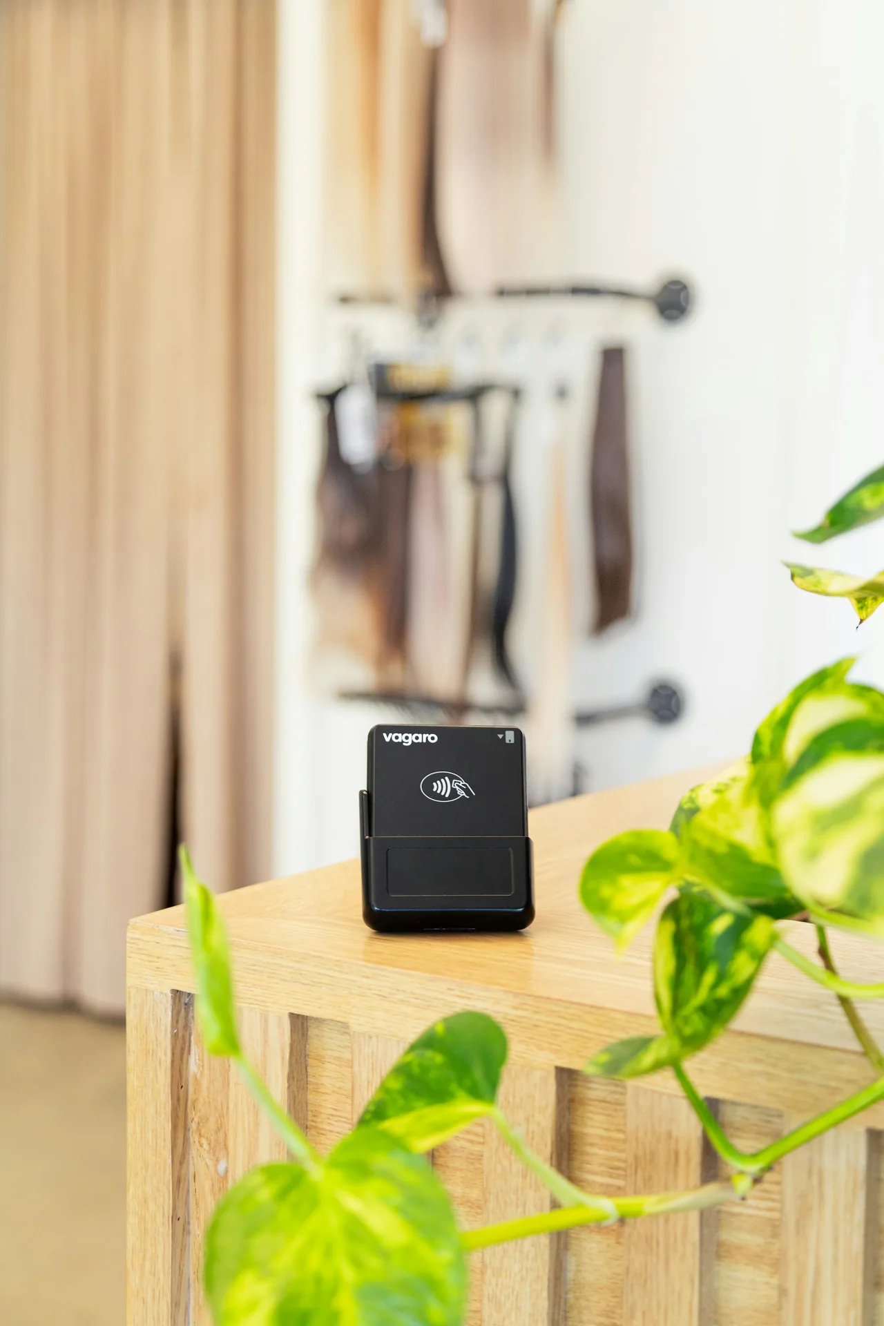 A black card reader stands on a wooden counter beside a green plant.