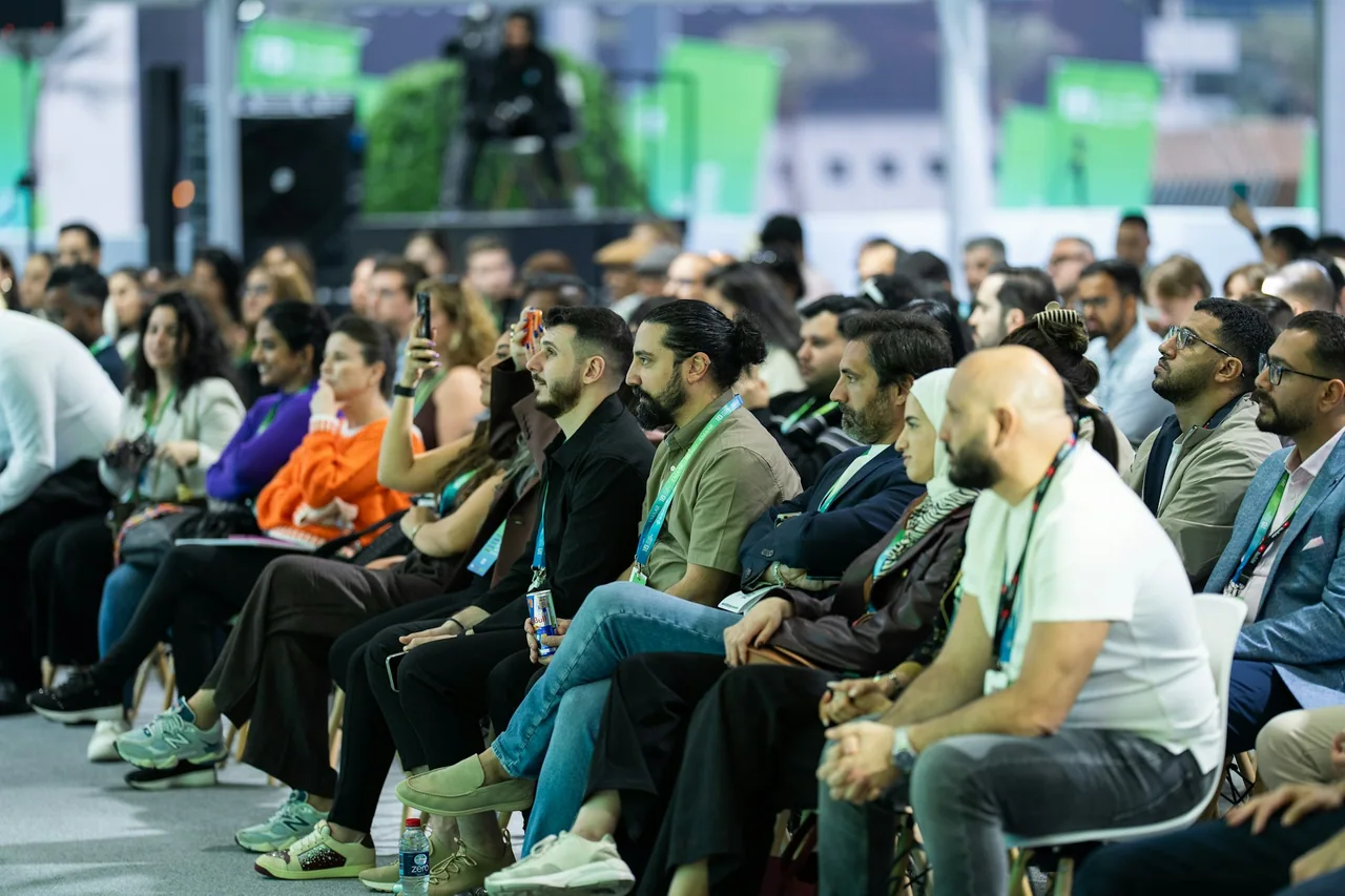 An audience sits in rows and watches a conference session.